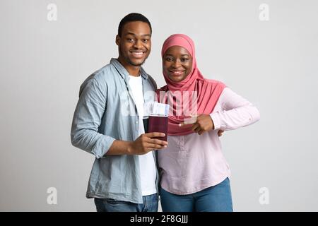 Couple souriant tenant des billets de vol et des passeports sur fond gris Banque D'Images