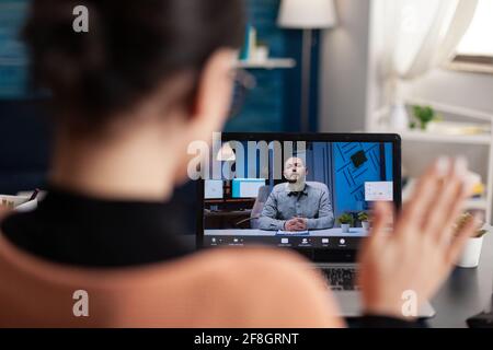L'élève accueille son professeur d'université lors d'une réunion virtuelle à l'aide d'un ordinateur portable. Webinar d'école de littérature de race blanche tout en étant assis à une table de bureau dans le salon Banque D'Images
