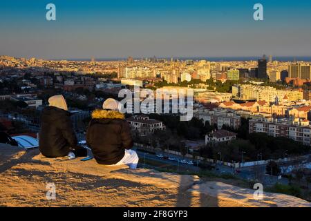 Vue arrière de deux personnes contemplant la ville à leurs pieds. Ils portent des sweats à capuche et des manteaux parce que c'est l'hiver. Barcelone, Catalogne, Espagne. Banque D'Images