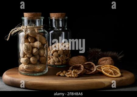 Deux bocaux en verre avec bouchons sont remplis de fruits secs, y compris des noix sur une planche à découper en bois Banque D'Images