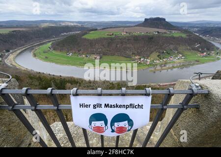 14 avril 2021, Saxe, Königstein: Un avis "les masques sont obligatoires ici" est suspendu sur la rambarde de la forteresse de Königstein en Suisse saxonne, avec l'Elbe et le Lilienstein en arrière-plan. Les portes de la forteresse historique sont ouvertes aux visiteurs depuis le 12 avril après plus de cinq mois de fermeture due à la couronne. Photo: Robert Michael/dpa-Zentralbild/ZB Banque D'Images