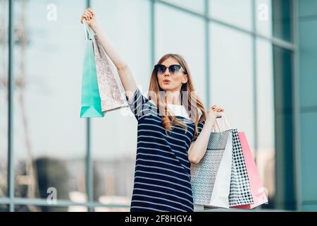 joyeuse bonne jeune femme aime faire du shopping, porte des sacs et court pour faire du shopping, dans le fond du centre commercial. Mode, shopping Banque D'Images