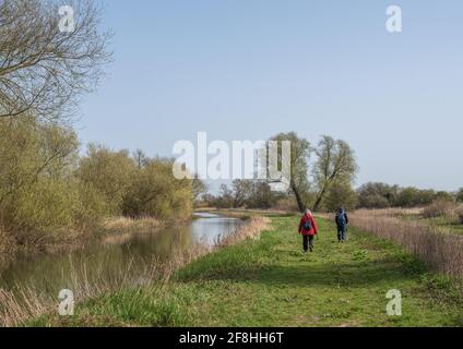 Couple senior marchant le long d'un chemin de remorquage sur un canal par une journée ensoleillée avec le ciel bleu. Banque D'Images