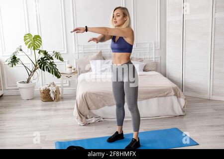 Athlétique belle femme est debout sur le tapis de yoga bleu dans des vêtements de sport élégants, faisant l'échauffement avant l'entraînement, l'entraînement à la maison. Femme sportive travaillant Banque D'Images
