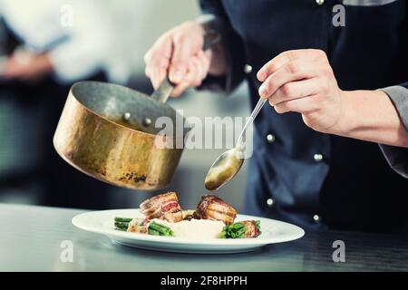 Chef pouring sauce sur plat dans une cuisine de restaurant, la récolte sur les mains, image filtrée Banque D'Images