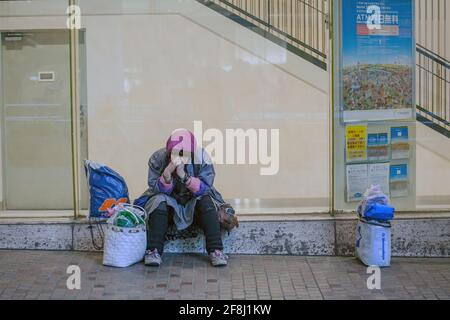 Une femme japonaise sans foyer est assise sur un mur couvrant la face, Shibuya, Tokyo, Japon Banque D'Images