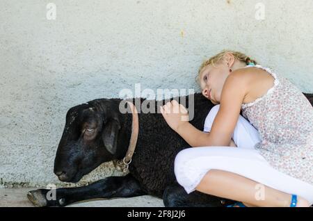 adorable petite fille blonde caressant la chèvre noire Banque D'Images