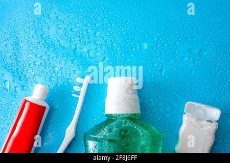 Concept de soins dentaires et d'hygiène buccale avec une bouteille de rince-bouche vert, brosse à dents, soie dentaire et tube de dentifrice imbibés de gouttes d'eau, isola Banque D'Images