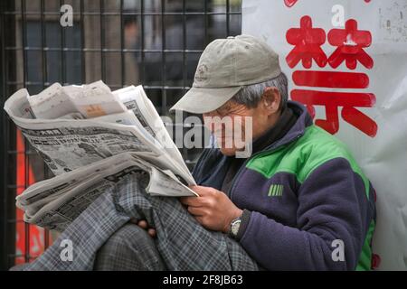 Un homme japonais sans-abri est assis à lire le journal sur le trottoir, Shinjuku, Tokyo, Japon Banque D'Images