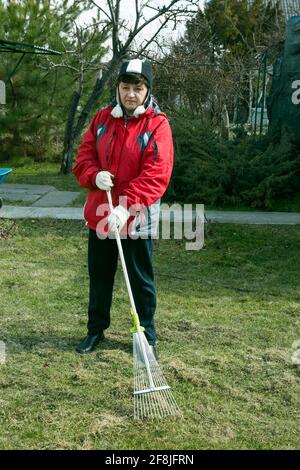 La femme travaille dans le pays. Aération et nettoyage de la pelouse avec un grand râteau. Jardinage pour améliorer la qualité de la pelouse et la croissance de l'herbe. Banque D'Images