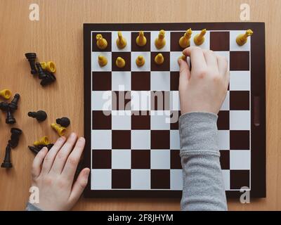 les mains des enfants organisent les échecs sur un échiquier vue de dessus de plus près Banque D'Images