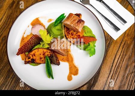 Steaks de filet de porc à la purée de pois et à la gousse de pois, citrouille cuite au four, croustilles de betteraves et feuilles de céleri, présentation décorative sur plaque blanche sur table en bois. Banque D'Images