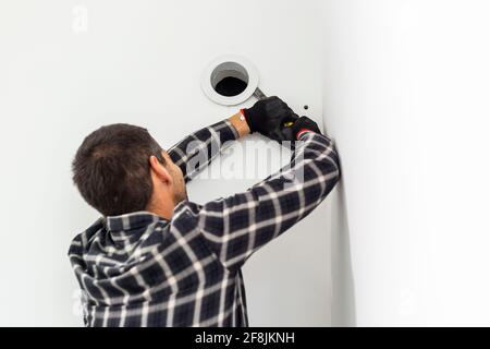 Le handyman avec son outil retire le couvercle de l'ouverture de ventilation dans le mur. Banque D'Images