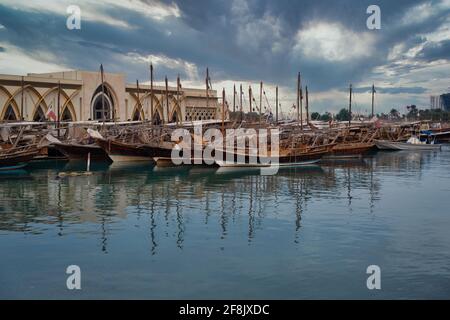 Vue sur la ville de Doha depuis la promenade de corniche, prise l'après-midi montrant des huws avec Drapeau du Qatar dans le golfe arabe en premier plan et nuages dans le ciel en arrière-plan Banque D'Images