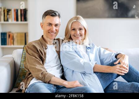 Portrait de couple mature amoureux. Un couple caucasien joyeux d'âge moyen passe du temps ensemble à la maison, se détendre sur un canapé dans la salle de séjour, vêtu de vêtements élégants et décontractés, souriant à l'appareil photo Banque D'Images