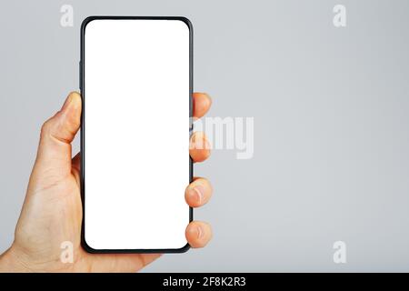 Tient la main d'un smartphone noir avec écran blanc vierge et design sans cadre moderne isolé sur fond gris. Placer pour le texte Banque D'Images