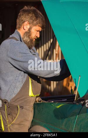 Un homme verse de l'huile de graissage dans la voiture. En été, dans la rue à côté de la maison. Banque D'Images