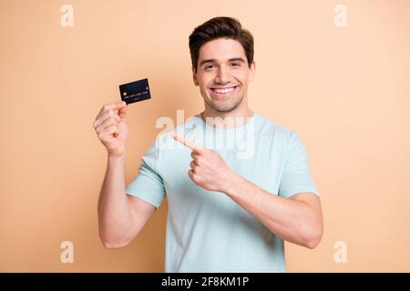 Portrait de gentil gai gars en utilisant tenue dans la main de démonstration solution de carte bancaire isolée sur fond beige pastel Banque D'Images