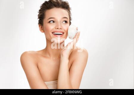Belle femme appliquant de la poudre sèche, en utilisant un coussin cosmétique sur sa peau faciale. Photo de femme avec maquillage parfait sur fond blanc. Concept de beauté Banque D'Images