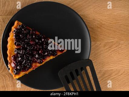 Tarte aux carottes et aux raisins de Corinthe saupoudrée sur une assiette noire et couverts une spatule pour la friture, partiellement présente dans le cadre, noire, sur un sanglier en bois Banque D'Images