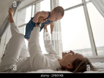 Portrait à la maison d'un bébé garçon avec mère sur le lit. Maman tenant et embrassant son enfant. Concept de fête des mères Banque D'Images