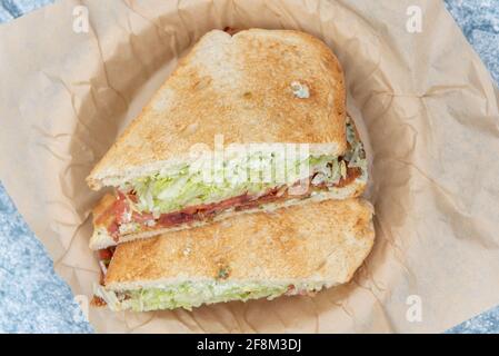 Vue de dessus du bacon, de la laitue, du sandwich aux tomates chargé de viande et de garnitures pressées entre deux tranches de pain de pâte aigre grillé. Banque D'Images