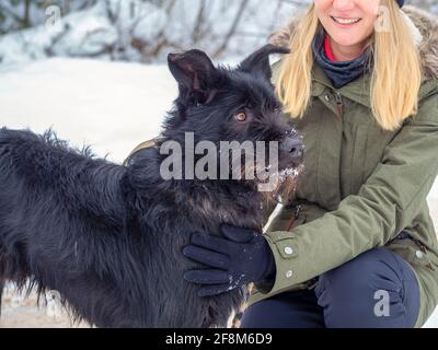 Jeune femme jouant avec drôle chien d'animal de compagnie noir avec la neige. Sur l'arrière-plan. Jouer avec la neige. Adorable chien appréciant son temps, l'hiver. Copier l'espace Banque D'Images