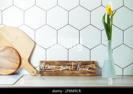 Vue de l'intérieur. Maison douce maison signe manuscrit sur le comptoir de cuisine à côté de tulipe jaune dans le vase et planches à découper sur le pavé hexagonal blanc Backgrou Banque D'Images