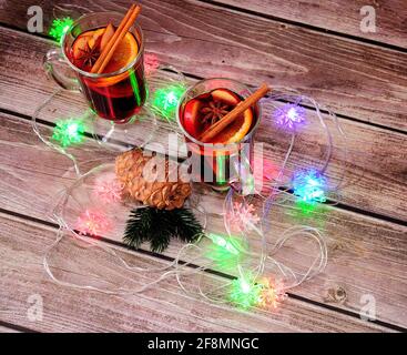 Deux verres de vin chaud aux épices, branches de pin avec un cône et guirlandes de Noël brûlantes sur une table en bois. Vue de dessus. Banque D'Images