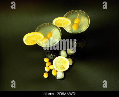 Deux verres de martini avec des tranches de citron et des olives sur fond noir à côté des glaçons. Gros plan. Banque D'Images