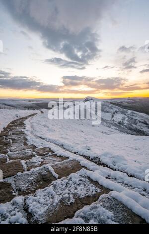 La neige glacée couverte sentier sinueux en pierre chemin menant vers le haut du côté de la montagne comme le soleil commence à venir au-dessus de l'horizon au lever du soleil matin d'hiver. Perspective. Banque D'Images