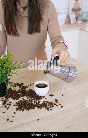 Une femme dans une cuisine scandinave légère verse le café d'un machine à café dans une tasse le matin Banque D'Images