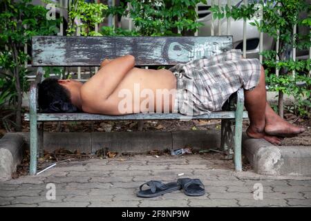 Vue sur un homme dormant sur un banc dans les rues de Bangkok. Banque D'Images