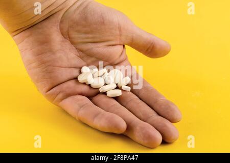 Mains et pilules médicales sur fond jaune. Diverses pilules blanches se trouvent dans la paume ouverte de la main d'un homme. Concept de santé et de médecine. Gros plan. Sélectionnez Banque D'Images