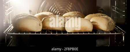 Petits pains de levain fraîchement cuits avec croûte croustillante sur métal grille dans le four de boulangerie Banque D'Images