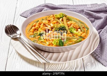 curry de noix de coco végétarien avec pois chiches, haricots verts, chou-fleur et brocolis dans un bol sur une table en bois blanc, cuisine indienne Banque D'Images