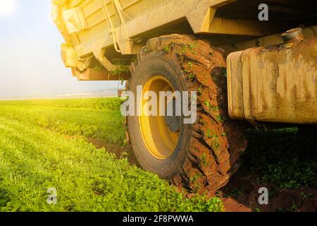 Concept d'agriculture. Roue du tracteur recouverte de boue et labourage sur le terrain en arrière-plan. Banque D'Images