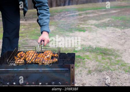 barbecue dans la nature au printemps. une main d'homme tient une grille de viande sur les charbons. Banque D'Images