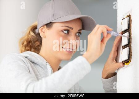 une femme installe une nouvelle prise dans le mur Banque D'Images