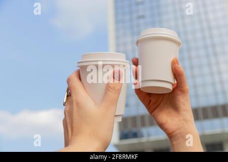 Deux tasses blanches avec café pour aller dans les mains des femmes sur fond de bâtiments de la ville et du ciel Banque D'Images