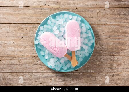 Des pop-glaces aux fraises et de la glace pilée sur une assiette bleue et du bois tableau Banque D'Images