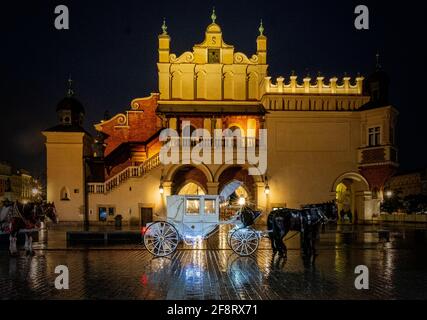 Des calèches blanches dessinées par des chevaux attendent de donner des manèges aux touristes dans la vieille ville de Cracovie, en Pologne la nuit. Banque D'Images