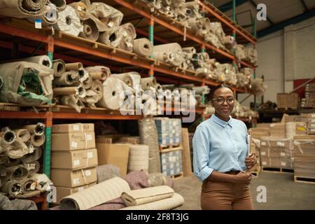 Jeune femme africaine souriante debout avec un presse-papiers dans un entrepôt Banque D'Images