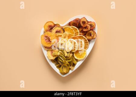 Prunes de fruits, kiwi, pêche, copeaux d'orange en forme d'assiette de coeur sur fond beige, séchage à la maison. En-cas végétalien gratuit. Vue de dessus. Banque D'Images