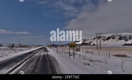 Vue sur l'entrée du village de la petite ville Kirkjubaejarklaustur dans le sud de l'Islande, le jour d'hiver ensoleillé avec route couverte de glace et indication du nom du lieu. Banque D'Images