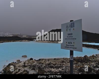 Panneau d'avertissement près de la centrale géothermique de Svartsengi informant de la température élevée de l'eau chaude dans les bassins de couleur bleue entre les roches de lave. Banque D'Images