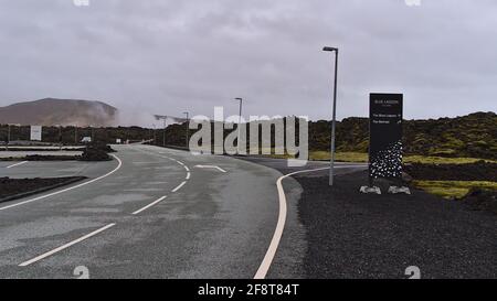 Vue sur la route d'accès vide à la station touristique Blue Lagoon situé entre les champs de lave dans la zone volcanique de Svartsengi avec logo et panneau directionnel. Banque D'Images