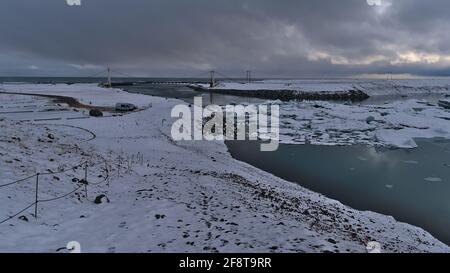 Belle vue sur le sud du glacier lagon Jokulsarlon avec parking, pont suspendu et icebergs flottants par jour nuageux en hiver. Banque D'Images