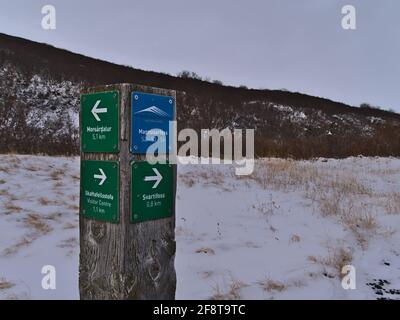 Panneau en bois à côté du chemin de randonnée dans le parc national de Vatnajökull en hiver montrant la direction de la cascade de Svartifoss avec des montagnes enneigées. Banque D'Images