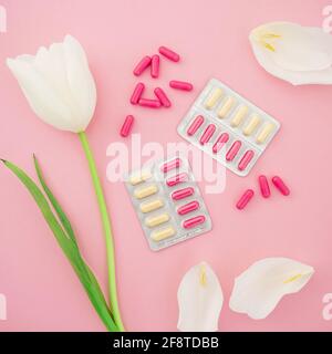 Composition médicale avec des comprimés de vitamines et des fleurs blanches sur fond rose. Flat lay, vue de dessus. Banque D'Images